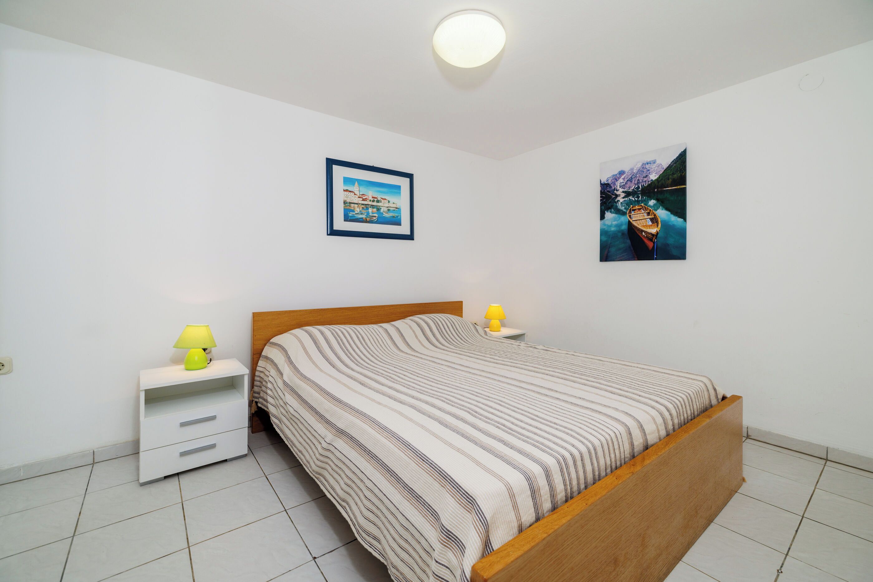 A bedroom with a wooden bed, white nightstands, a striped bedspread, and two wall-mounted lamps.