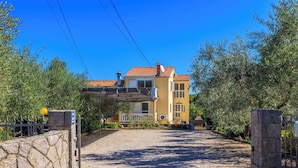 Ein zweistöckiges Haus mit roten Ziegeln, einer Steinsäule links und einer Schotterzufahrt zu einem verschlossenen Eingang.