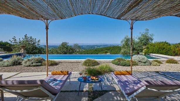 A poolside area with lounge chairs, a table with a bowl of fruit and drinks, and a view of a large pool and landscape. - Montelodoli Capanna, Gaiole in Chianti, Siena and Chianti (Gaiole in Chianti)