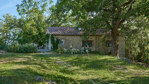 A rustic stone house with a tiled roof, surrounded by lush greenery and a small outdoor seating area with metal chairs. - Montelodoli Capanna, Gaiole in Chianti, Siena and Chianti (Gaiole in Chianti)