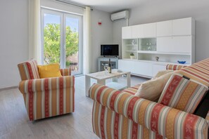 Un salon avec des canapés à rayures, une table basse, un téléviseur et un meuble blanc avec des étagères.