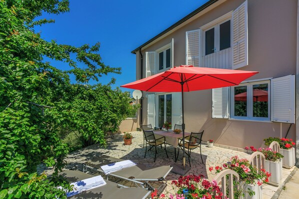 Eine Terrasse mit Tisch, Stühlen, einem roten Sonnenschirm und Kübelpflanzen.