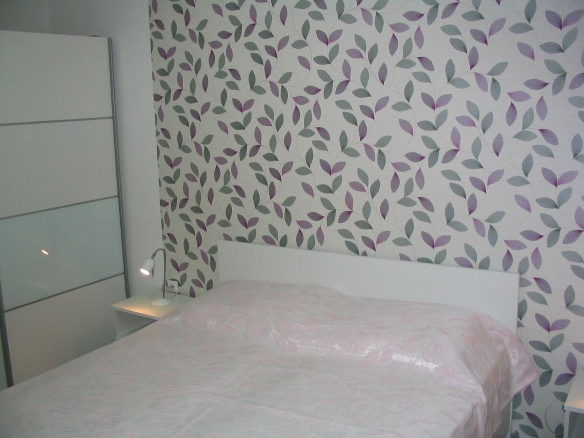 A bedroom with a bed, a wardrobe, and a wall with a leaf pattern.