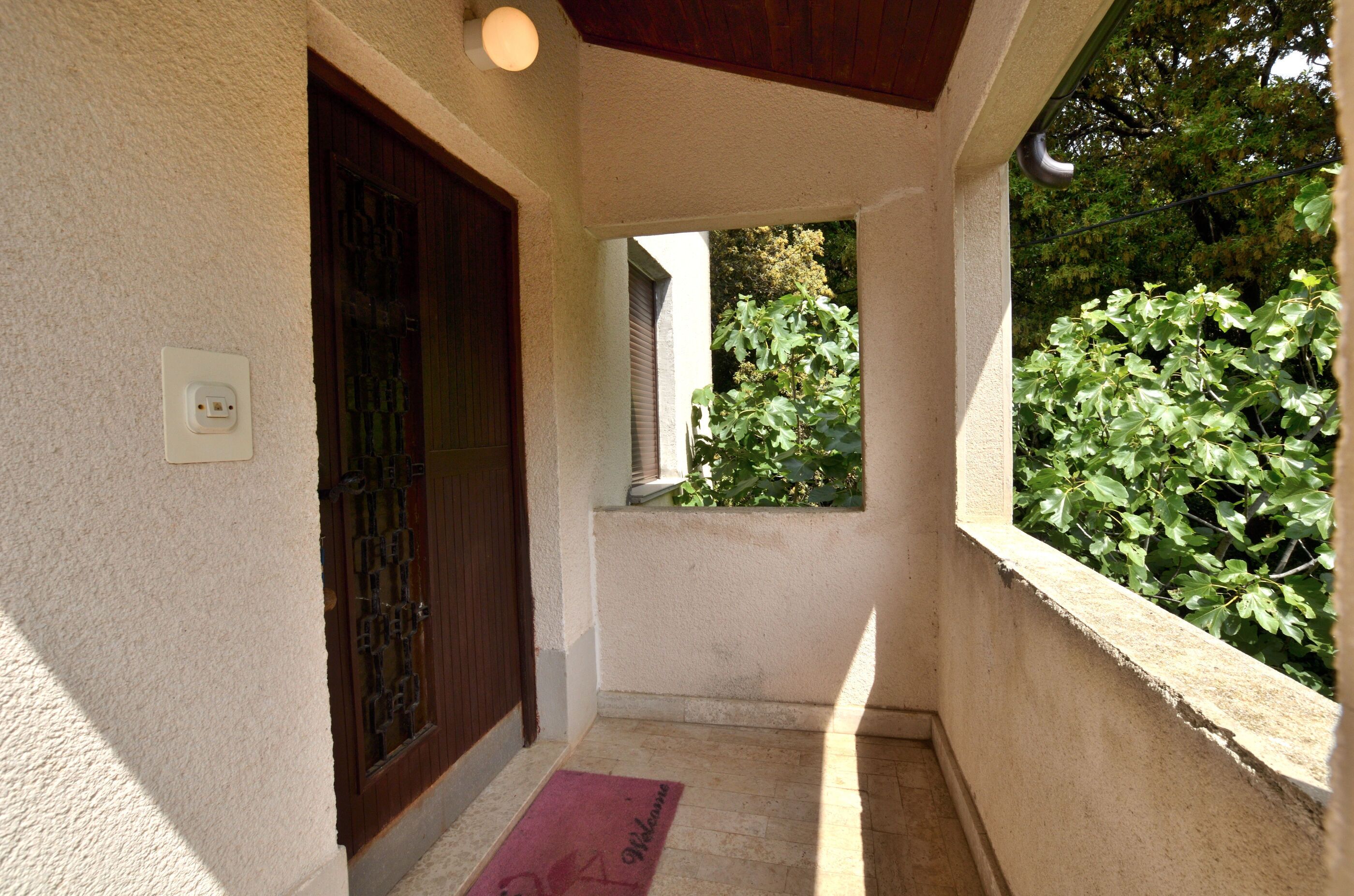 A narrow corridor with a wooden door, a small window, and a welcome mat.