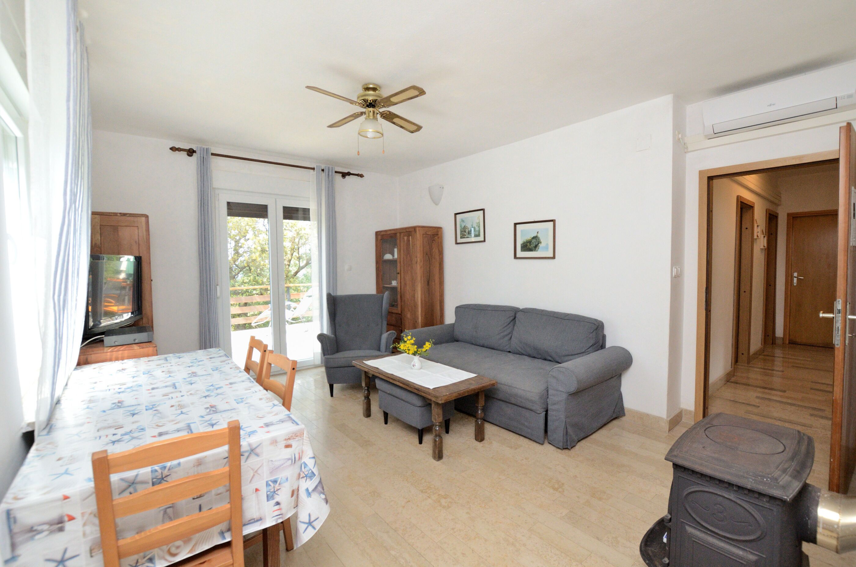 Ein Wohnzimmer mit einer Couch, einem Tisch mit Stühlen, einem Deckenventilator und einem Kaminofen.