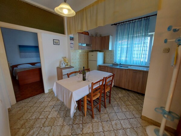 A compact kitchen with a dining table, chairs, a refrigerator, and a window with curtains.