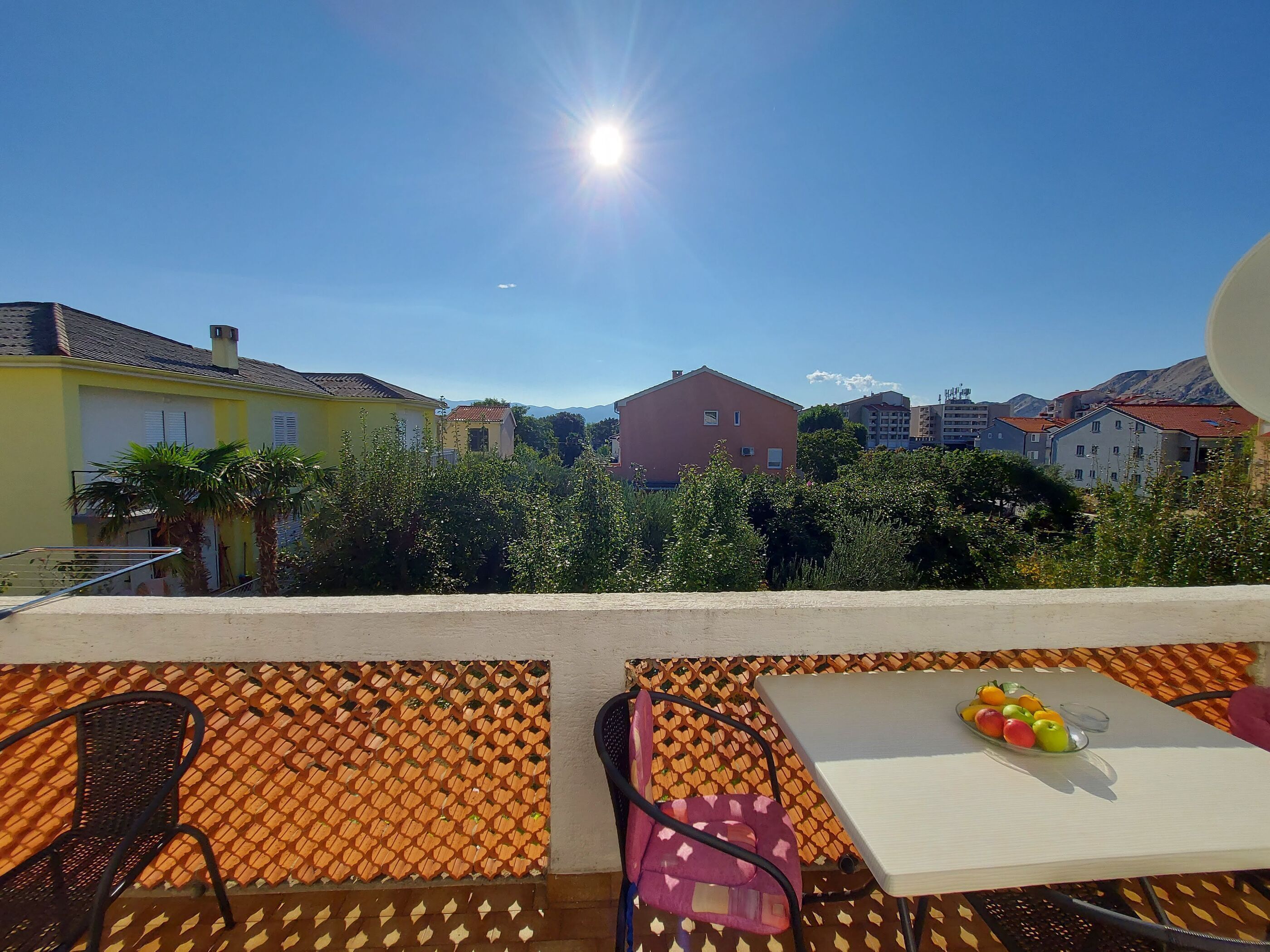 A balcony with a table, chairs, and a fruit bowl.