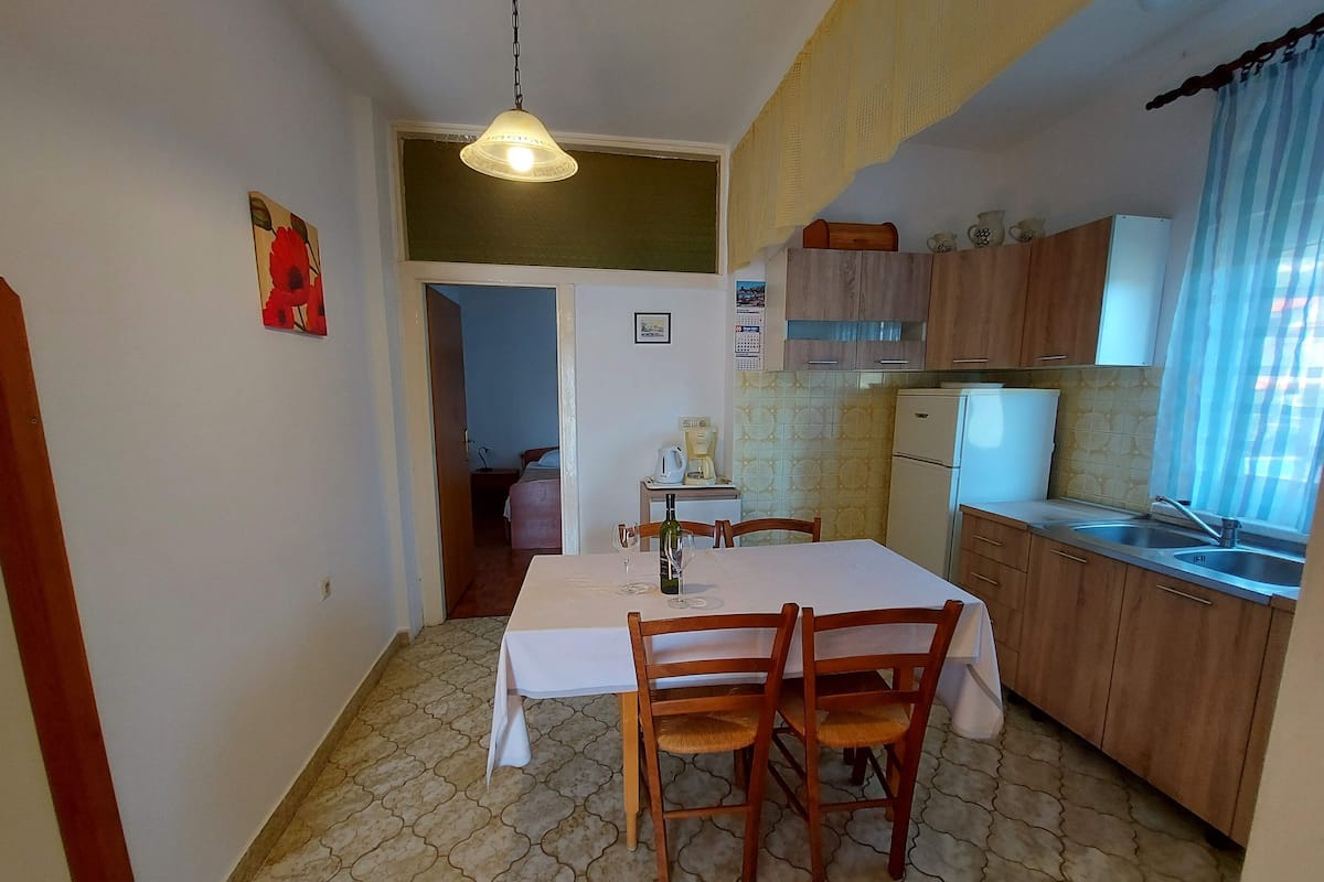A compact kitchen with wooden cabinets, a dining table with chairs, and a small refrigerator.