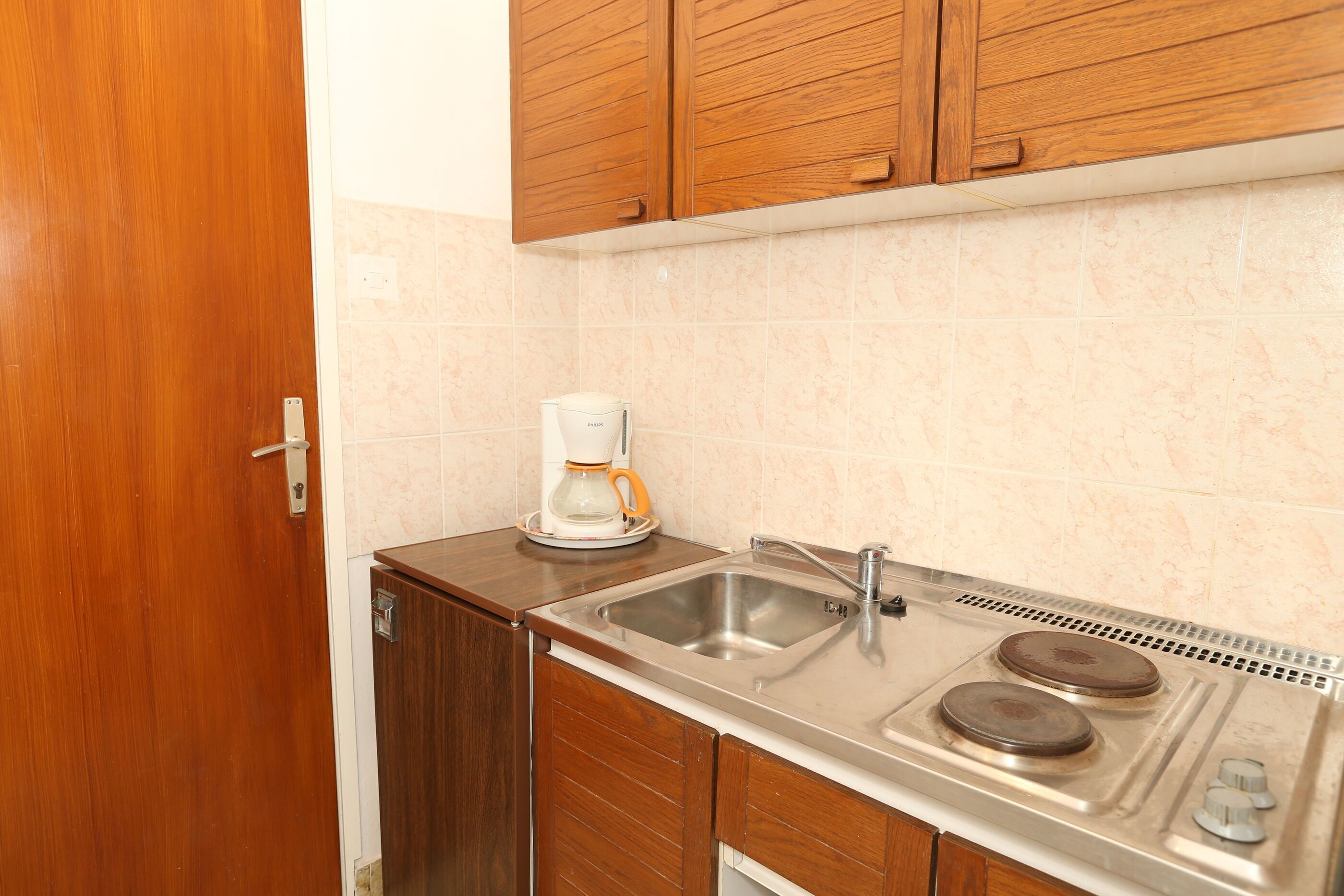 A compact kitchen with wooden cabinets, a stainless steel sink, and a coffee maker.