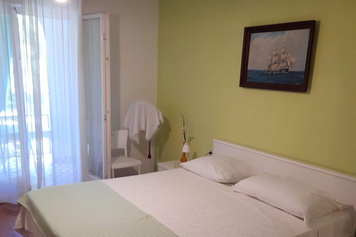 A hotel room with a large bed, a nightstand, a chair, and a painting on the wall.
