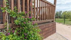 Une terrasse en bois avec une rambarde, entourée de verdure et de fleurs.