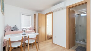 Une chambre moderne avec un lit, une table de chevet et des chaises. Une porte donne accès à une salle de bain avec une douche.