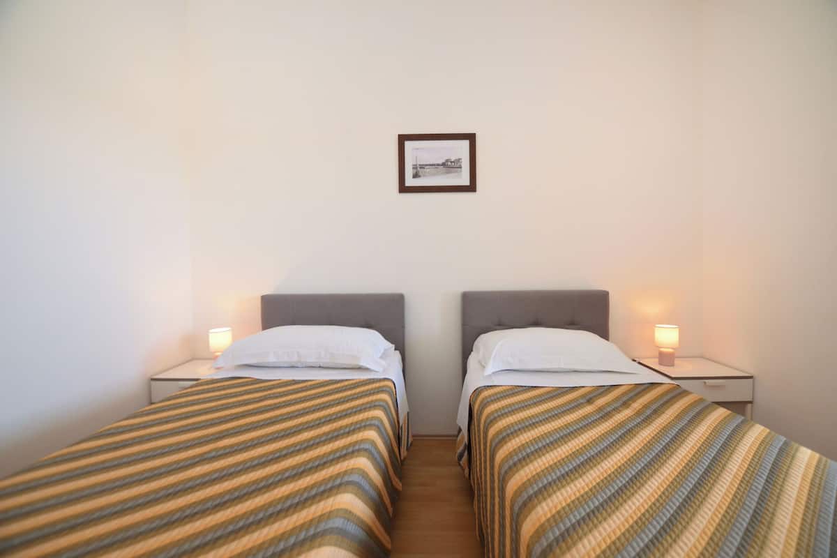 A twin room with two beds, each with a striped bedspread and white pillows, two bedside tables with lamps, and a framed picture on the wall.