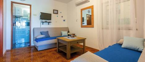 A room with a sofa, a small table with a bottle and glasses, a clock, and a mirror on the wall.