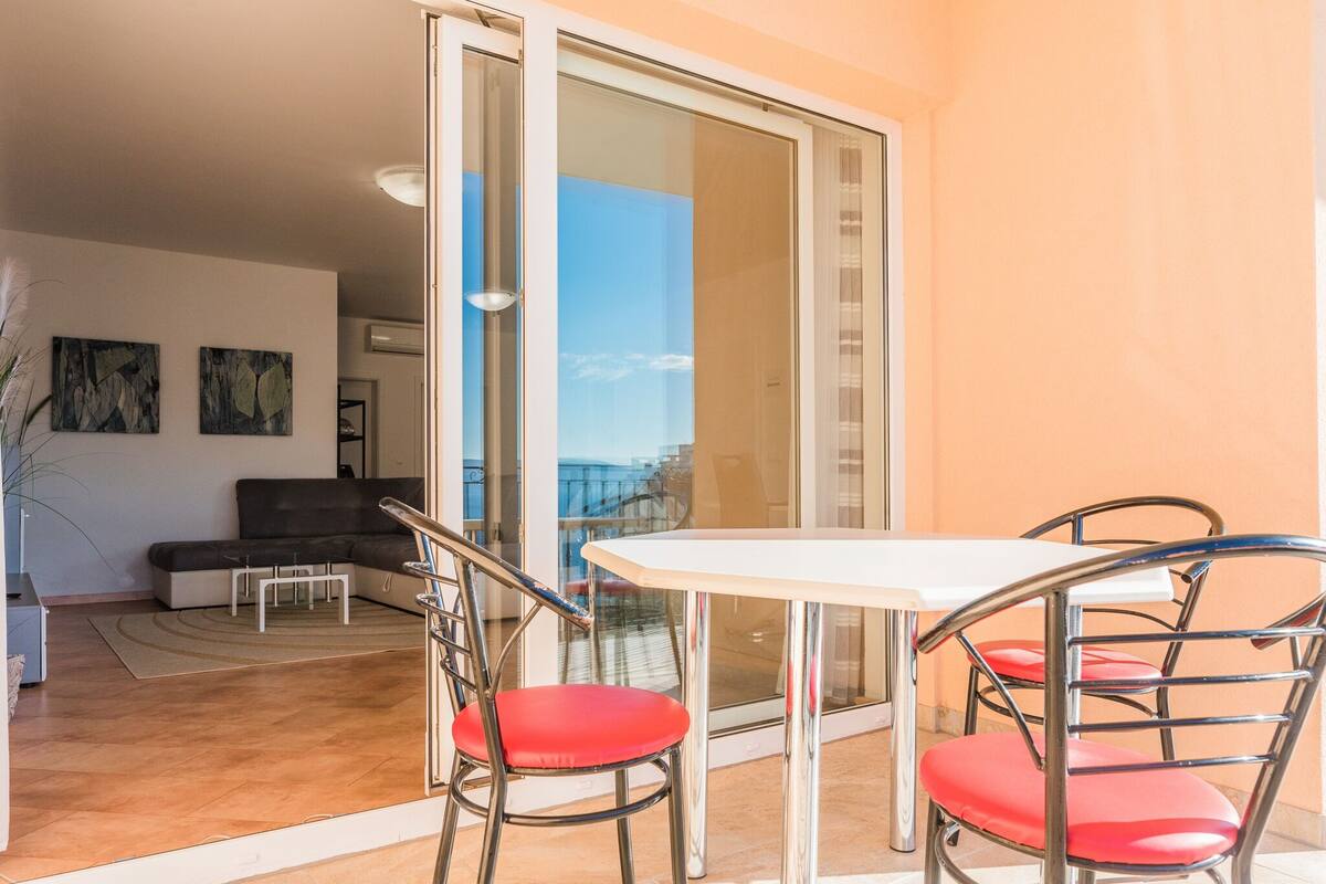 A balcony with a glass door, a white table, and red chairs.