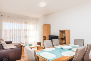 A modern living room with a sofa, a dining table with chairs, a TV, and a cabinet. - Apartments Marcel (Novi Vinodolski)