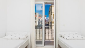 A room with two beds, a sliding glass door to an outdoor area, and a view of buildings and a mountain. - Apartments Marcel (Novi Vinodolski)