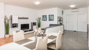 A modern living room with a dining area, featuring a flat-screen TV, a sofa, and a coffee table with candles. - Apartments Marcel (Novi Vinodolski)