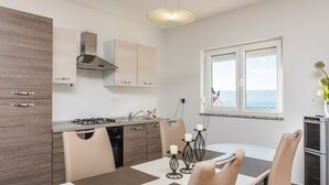 A modern kitchen with a gas stove, a built-in oven, and a window with a view of the sea. - Apartments Marcel (Novi Vinodolski)