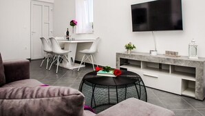 A modern living room with a flat-screen TV, a dining area with white chairs, a round black coffee table, and a grey sofa. - Apartments Zdeslav (Rogoznica)
