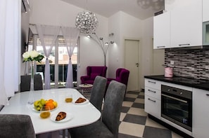 Eine moderne Küche mit weißen Schränken, einer schwarzen Arbeitsplatte und einem eingebauten Backofen. Es gibt einen Essbereich mit einem weißen Tisch, grauen Stühlen und einer Vase mit Blumen.