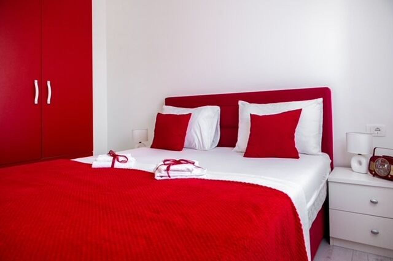 Una habitación de hotel con una decoración en rojo y blanco, que incluye una cama con ropa de cama roja y blanca, un cabecero rojo y una mesita de noche blanca con un radio.