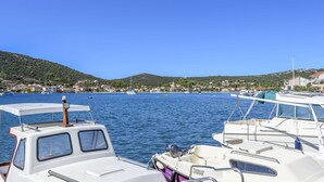 Un puerto deportivo con barcos amarrados, agua tranquila y un pueblo con colinas al fondo.