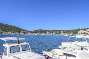 A marina with boats docked, calm water, and a hilly town in the background. - House Nanci (Vinisce)
