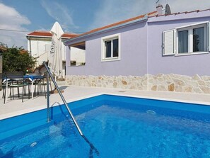 A swimming pool with a ladder, a stone wall, and a building with windows and a door. - House Nanci (Vinisce)