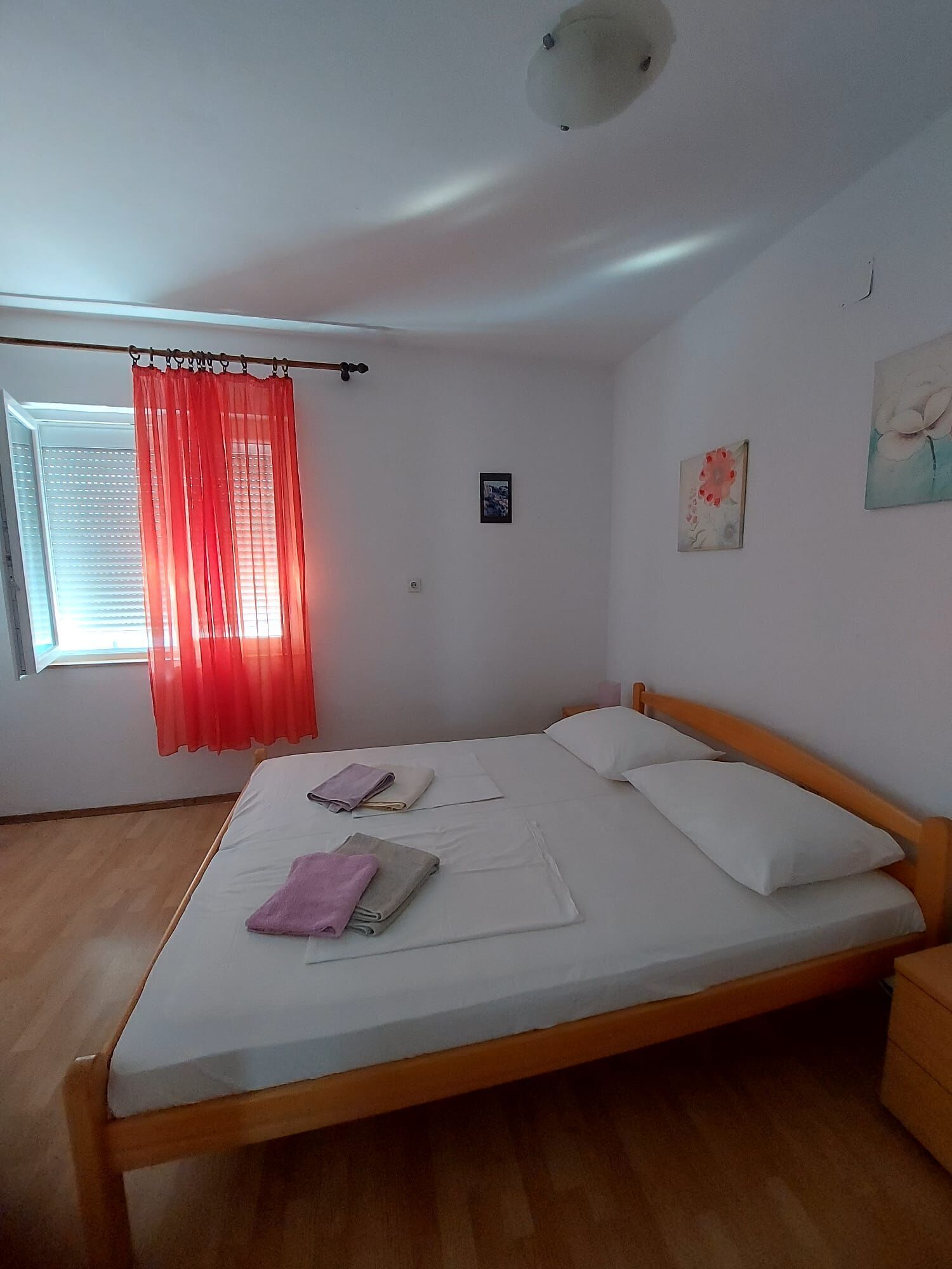 A bedroom with a single bed, a window with blinds, a red curtain, and a ceiling light fixture.