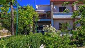 Un edificio di due piani con antenne paraboliche, un balcone e un giardino con diverse piante.