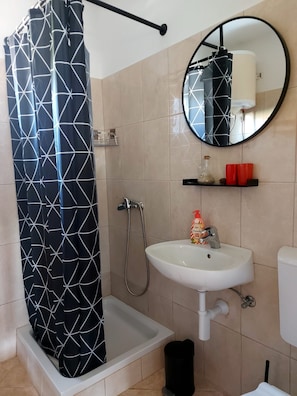 A bathroom with a shower, a sink, a toilet, a mirror, and a shelf with toiletries. - Apartments Slavica (Banjol)