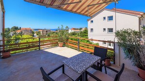 Un balcone con tavolo e sedie, piante in vaso e vista sul mare e sugli edifici.