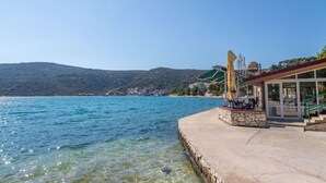 A waterfront hotel with a concrete deck, outdoor seating, and a view of the sea and hills. - Apartments Sea Star Ivana (Marina)