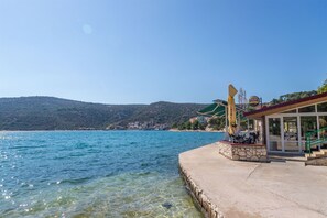 A waterfront hotel with a concrete deck, outdoor seating, and a view of the sea and hills. - Apartments Sea Star Ivana (Marina)