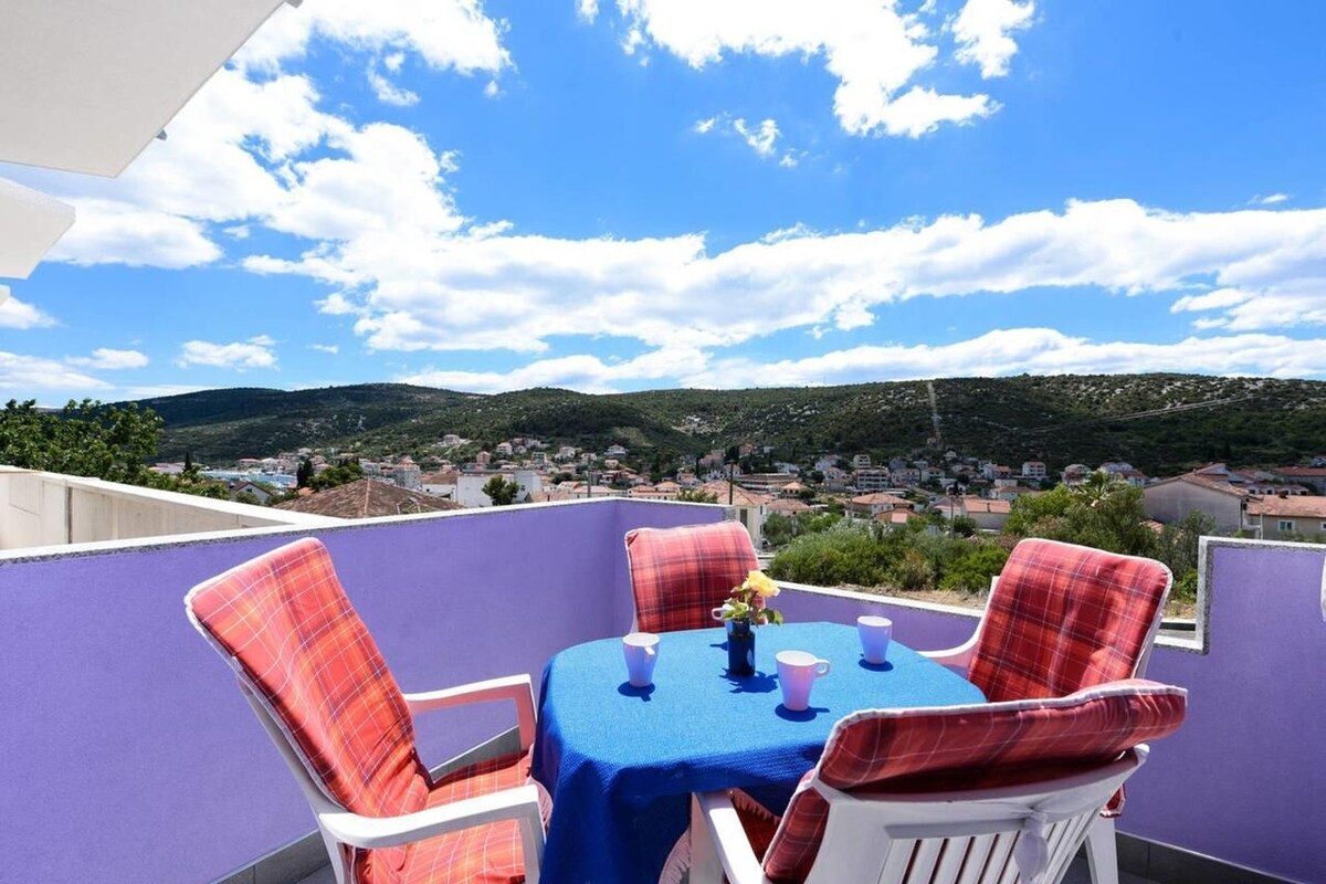 A terrace with a table and chairs, a view of a town and hills in the background.