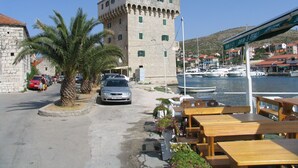 A coastal town with a prominent stone tower, a marina with boats, and outdoor seating by the water. - Apartments Sea Star Ivana (Marina)