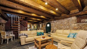 A cozy living room with a stone wall, wooden ceiling beams, and a staircase leading to an upper level. - Villa Romantic (Bribir)