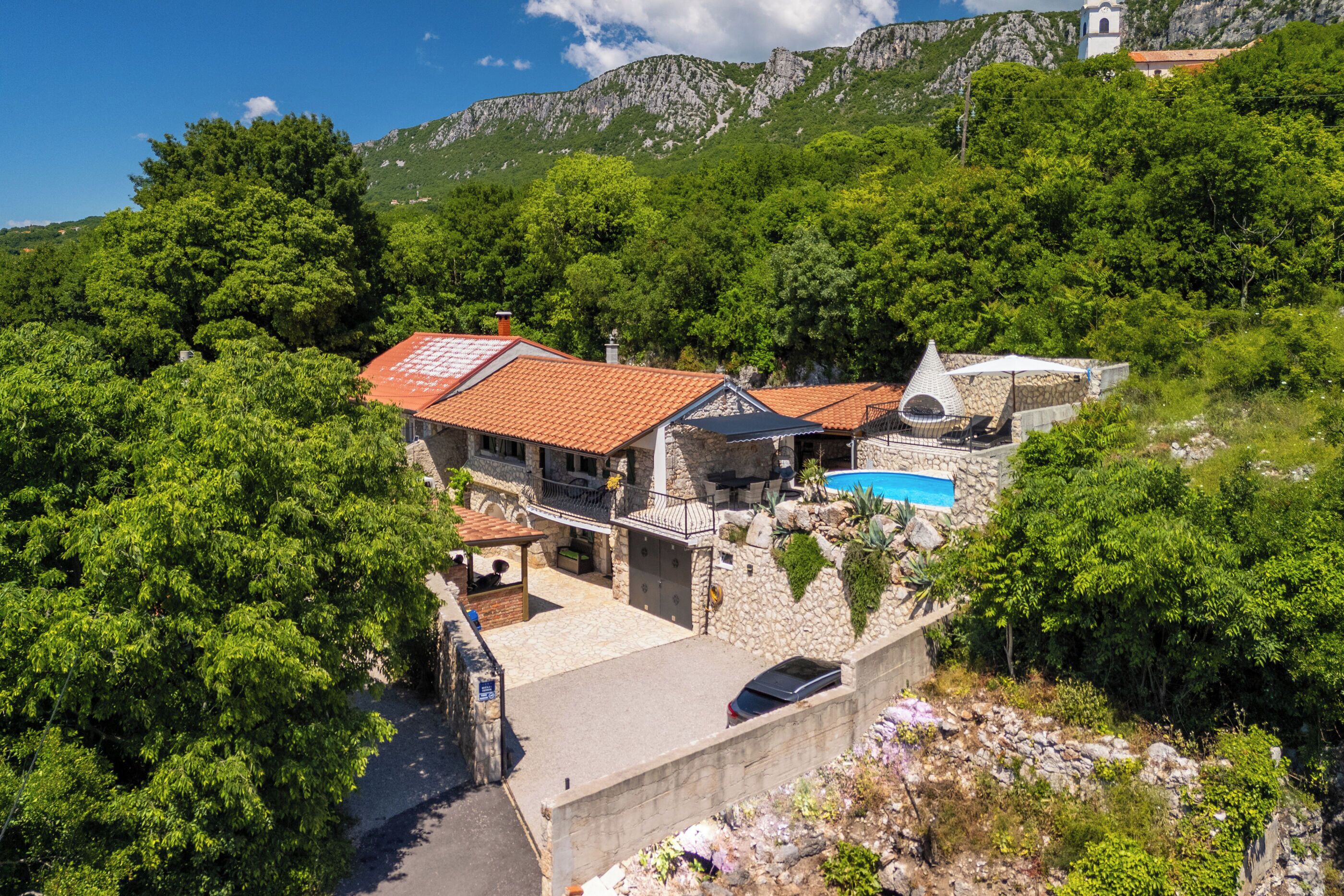A hillside villa with a swimming pool, stone walls, and a red-tiled roof.