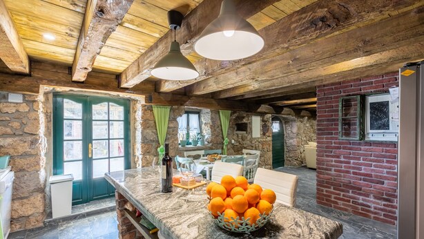 A rustic kitchen with a stone wall, wooden ceiling beams, and a marble countertop with a bowl of oranges. - Villa Romantic (Bribir)