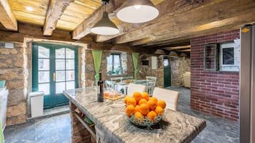 A rustic kitchen with a stone wall, wooden ceiling beams, and a marble countertop with a bowl of oranges.