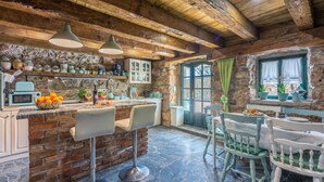 A rustic kitchen with exposed wooden beams, a stone wall, and a bar area with stools. - Villa Romantic (Bribir)