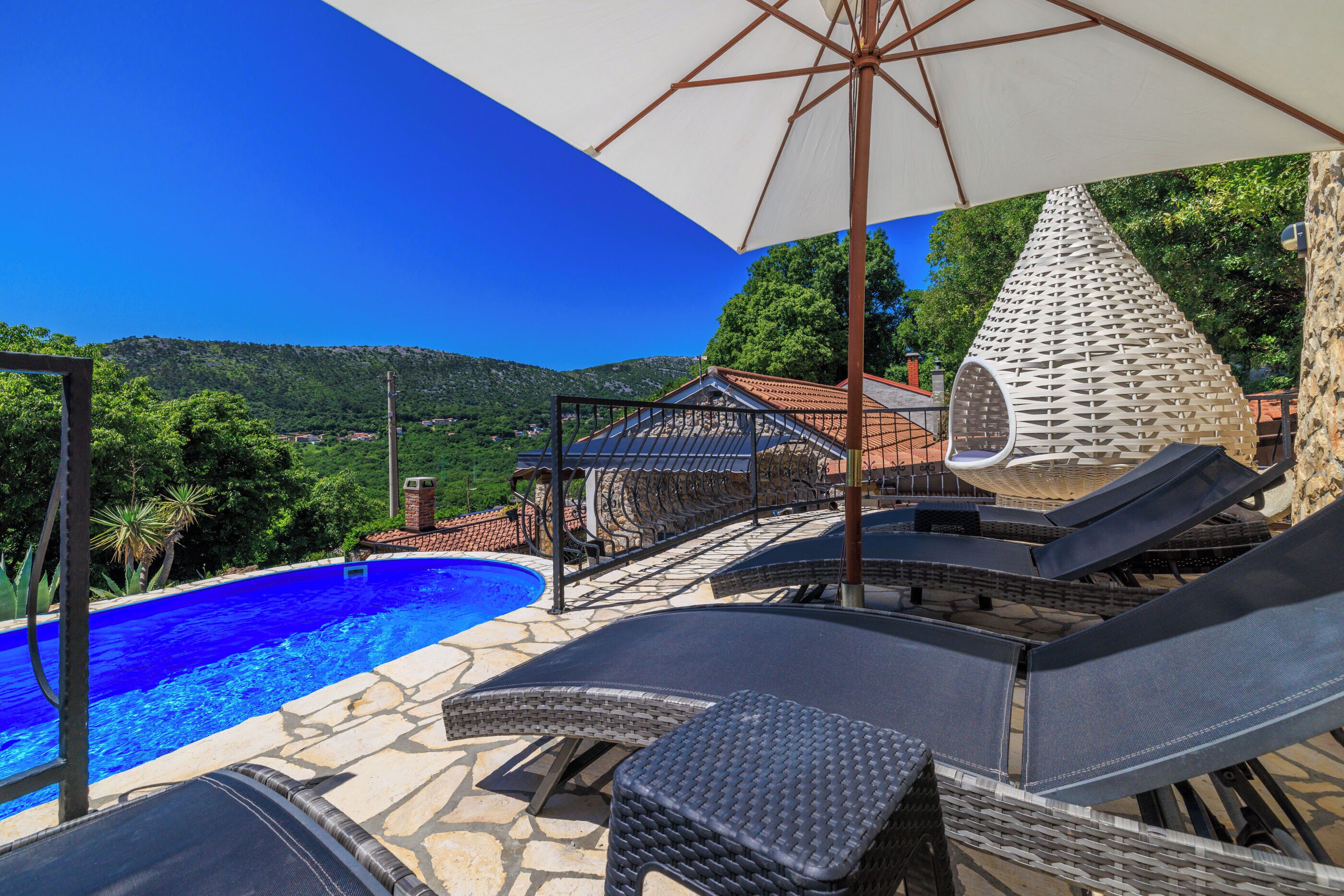 A poolside area with lounge chairs, a pergola, and a view of a mountain.