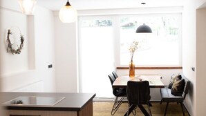 Une cuisine moderne dotée d’un îlot central, d’une table à manger avec des chaises et d’une grande fenêtre qui laisse entrer la lumière naturelle.
