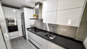 Een moderne keuken met witte kasten, een zwart aanrecht, roestvrijstalen apparatuur en een inbouwoven.