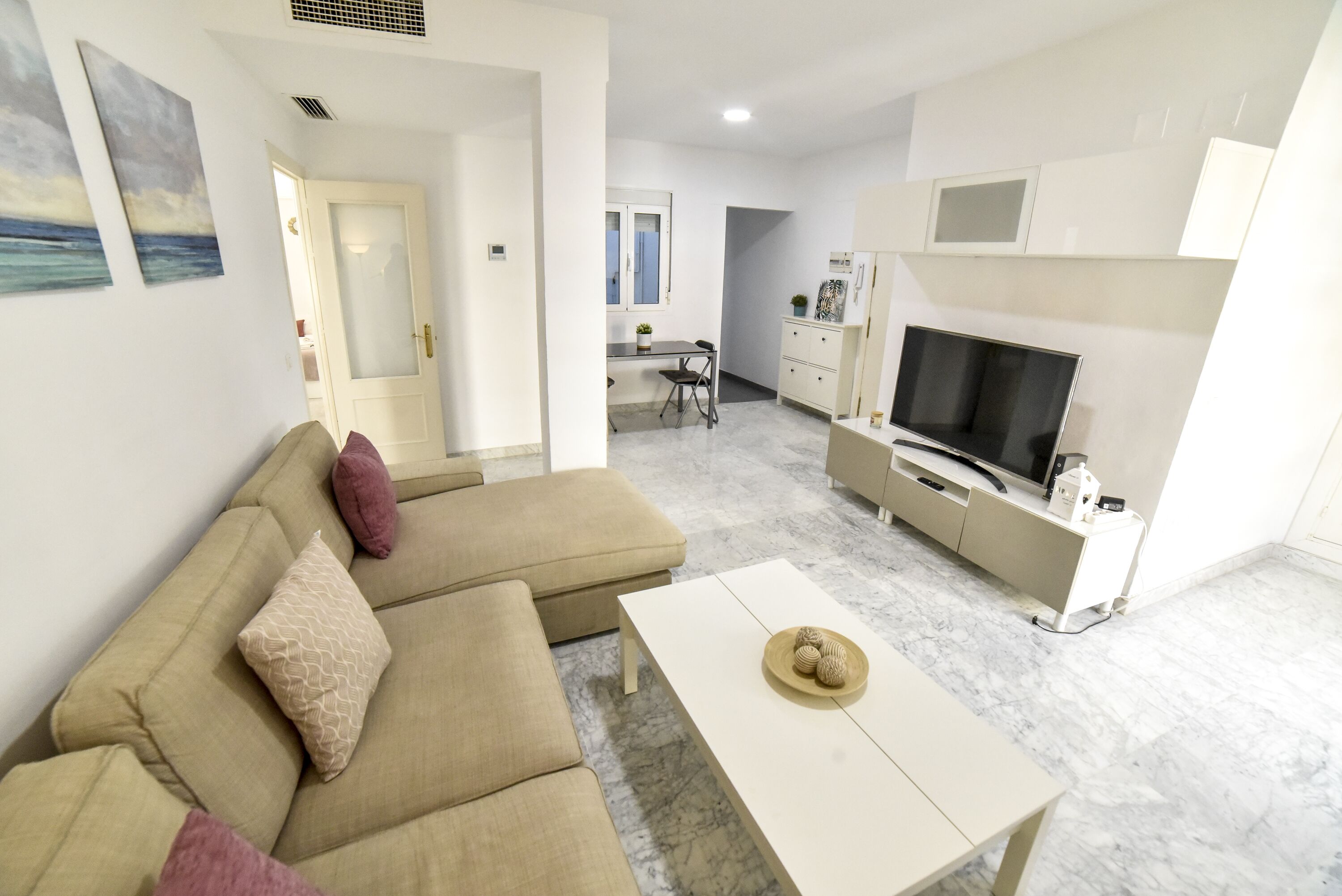A modern living room with a beige sofa, a white coffee table, and a TV stand.