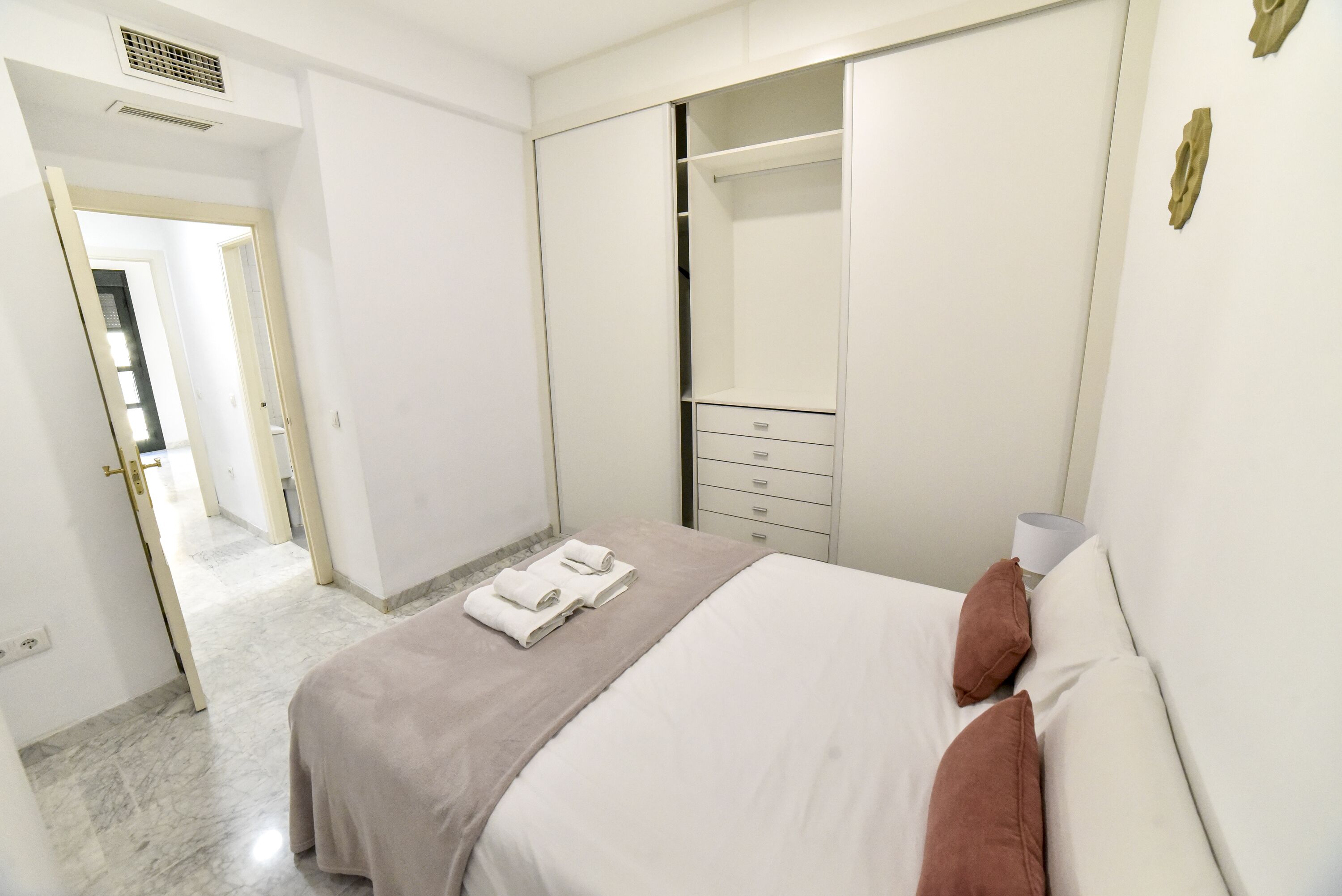 A hotel room with a bed, a wardrobe, a nightstand, and a bathroom visible through an open door.