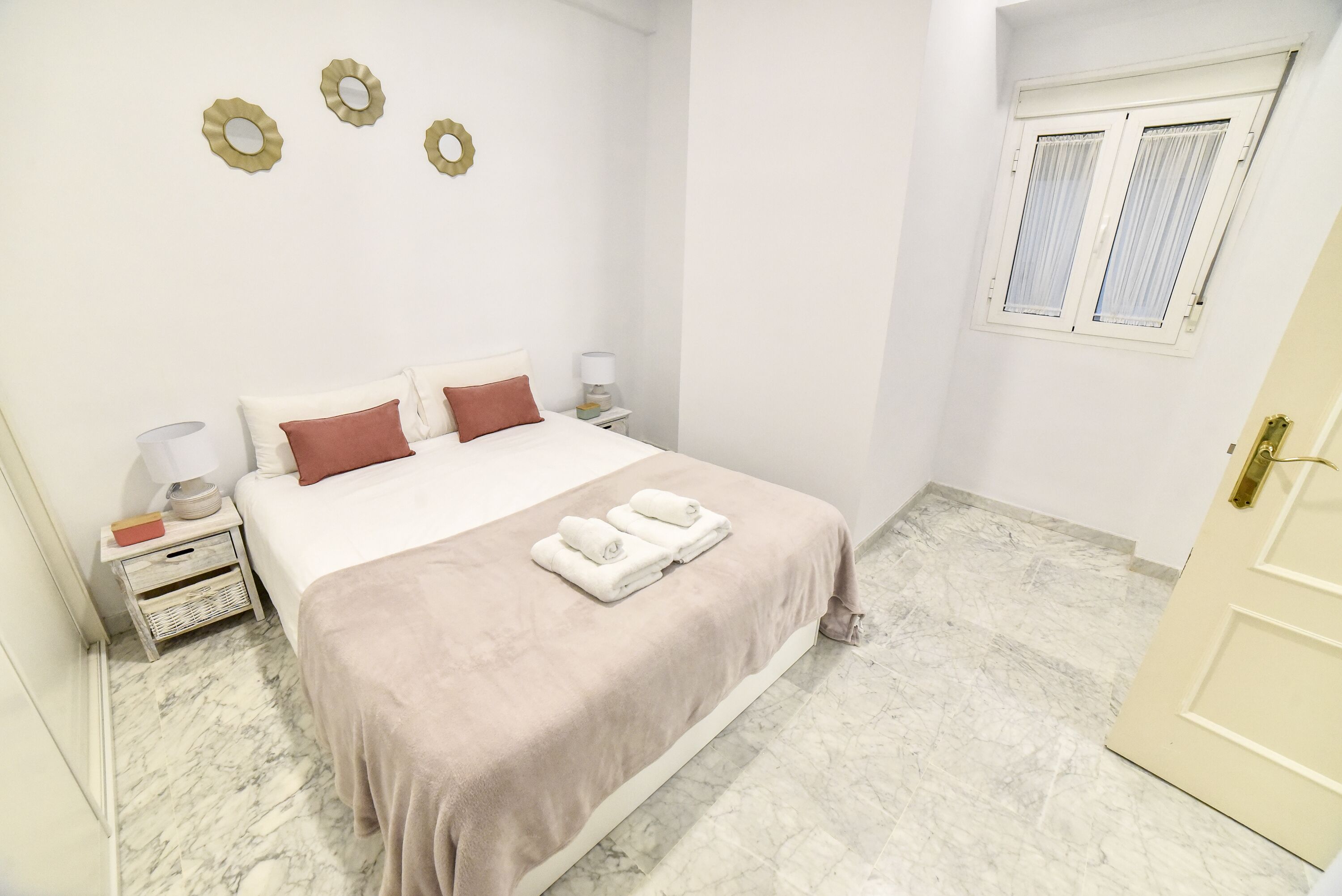 A neatly arranged bedroom with a bed, bedside tables, a window, and a door.