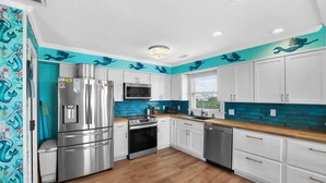 A modern kitchen with white cabinets, stainless steel appliances, and a teal backsplash. - OCEANFRONT- Hatteras Island/Salvo: 2 Primaries, Hot Tub, Large Open Living Space (Salvo)
