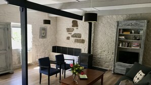 A cozy living room with a stone wall, a fireplace, a sofa, and a coffee table with flowers. - Holiday home LES TIARELLES (Commana)